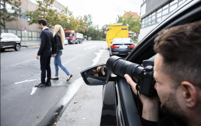 man in car secretly taking photos of man and woman walking across the street